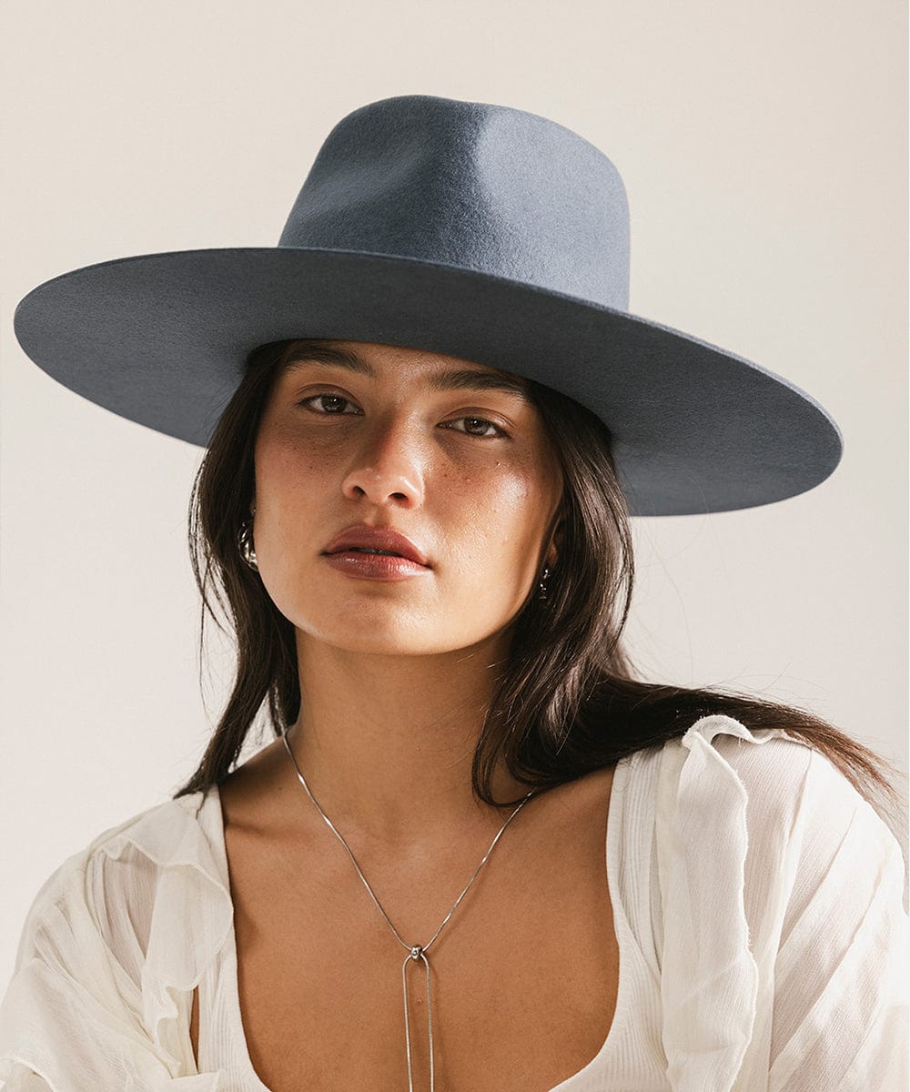 Woman wearing a vintage blue colored fedora hat and a white top against a plain background #color_vintage blue