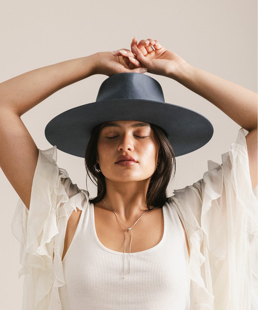 Woman wearing a vintage blue colored fedora hat and a white top, posing with her eyes closed against a plain background #color_vintage blue
