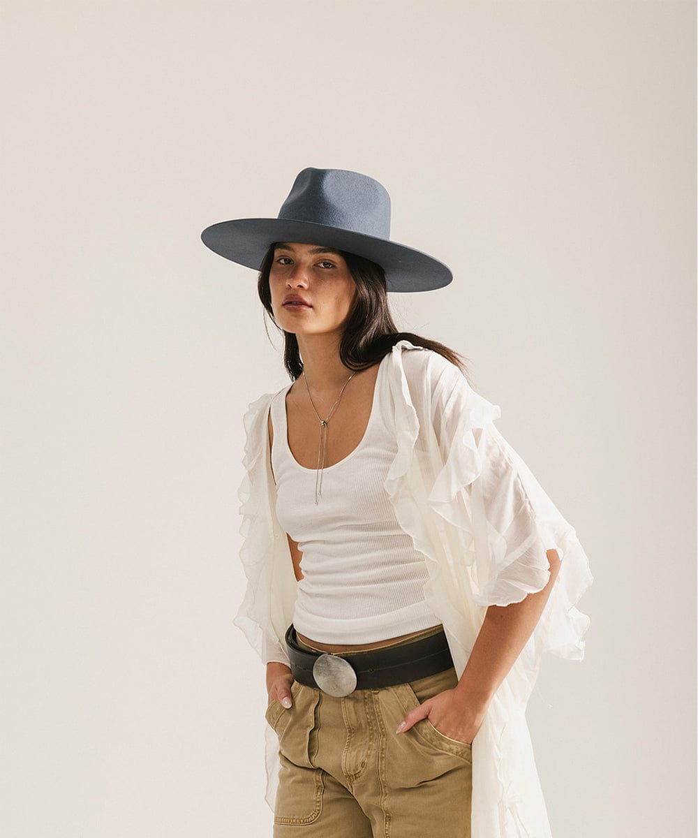 Woman wearing a white top, beige pants, and a vintage blue colored fedora hat against a plain background #color_vintage blue