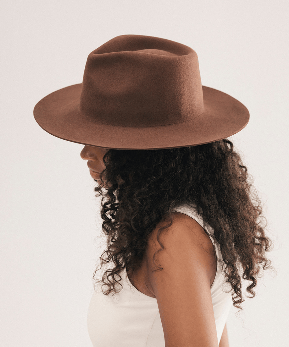 A woman in profile wearing a brown wide-brim fedora hat, shown against a plain light background #color_dark oak