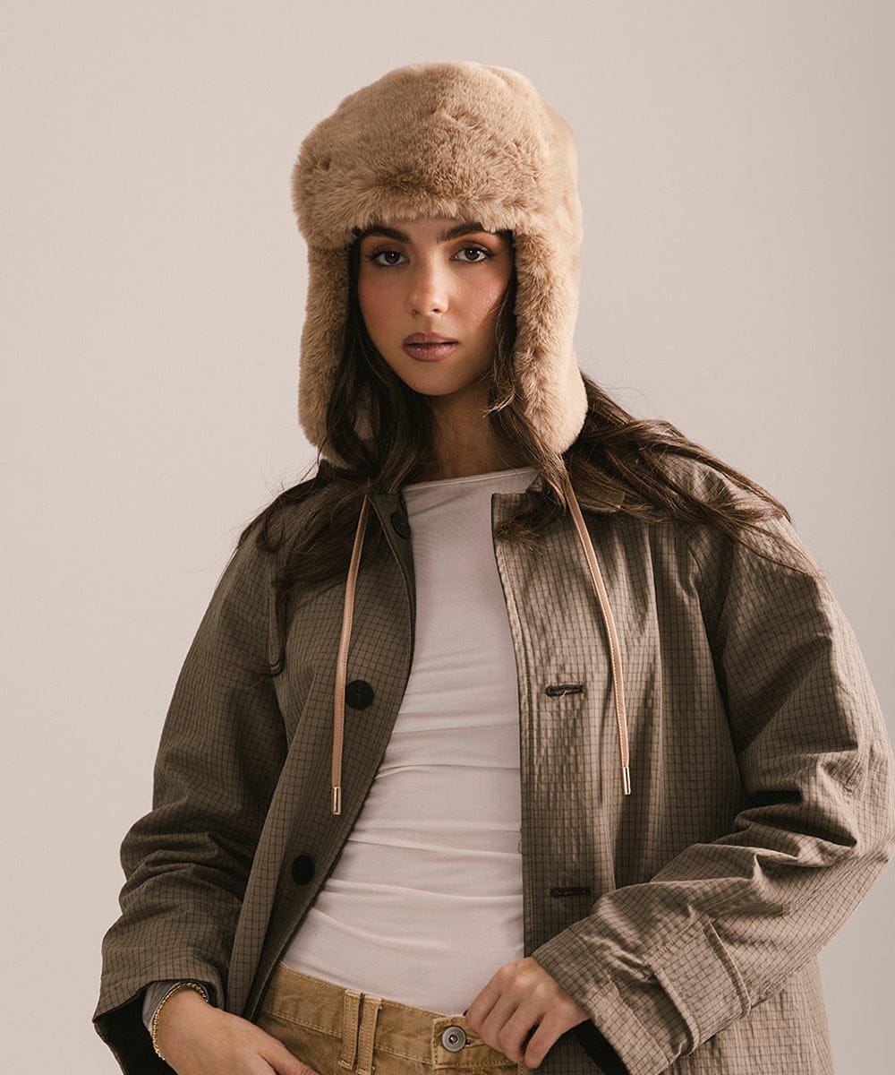 Woman wearing a fur-trimmed hat and coat against a plain background #color_tan