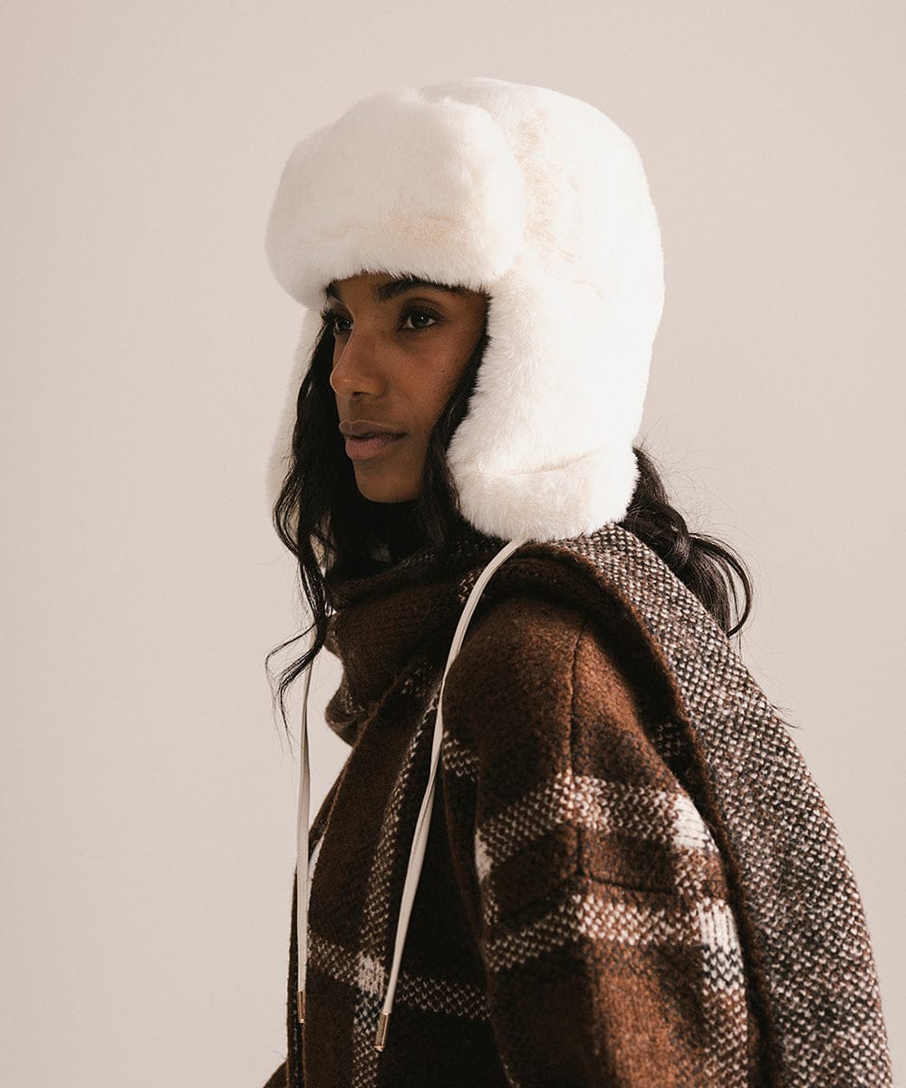 Person wearing a white fur-trimmed hat and brown coat against a plain background #color_winter white