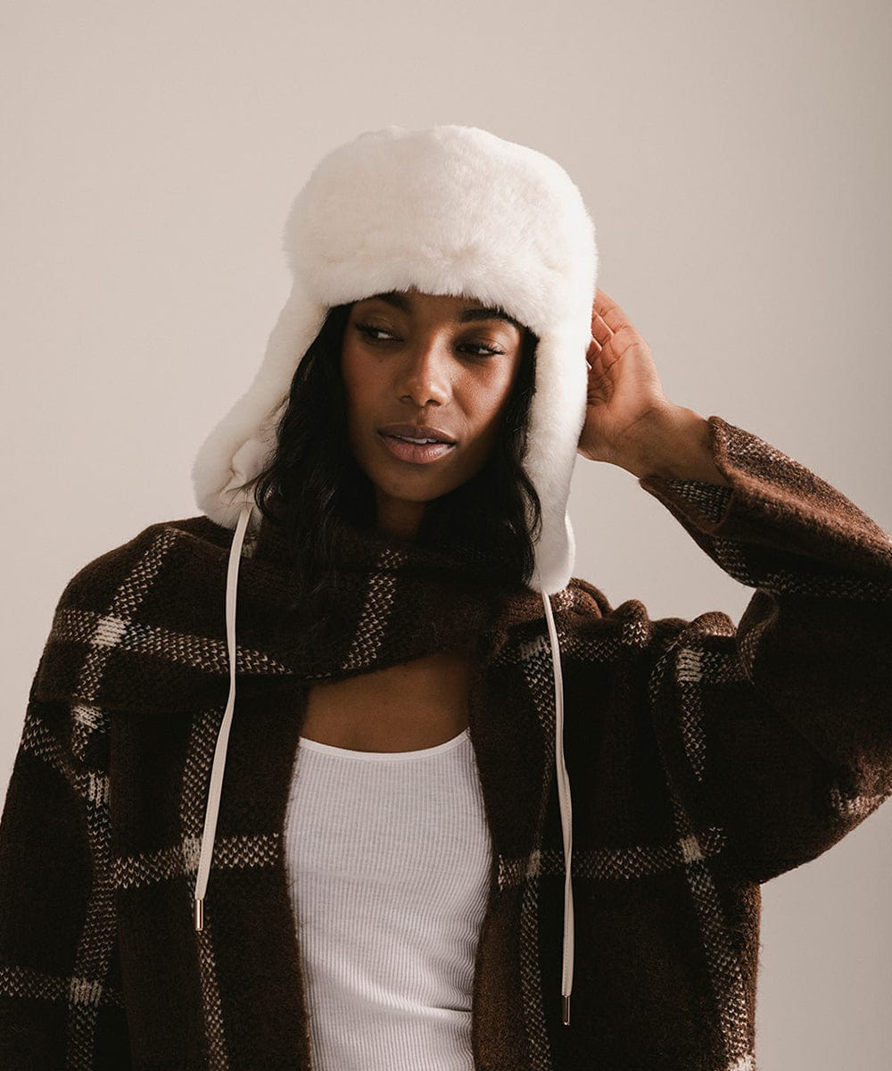 Woman wearing a white fur-trimmed hat and plaid coat against a neutral background #color_winter white