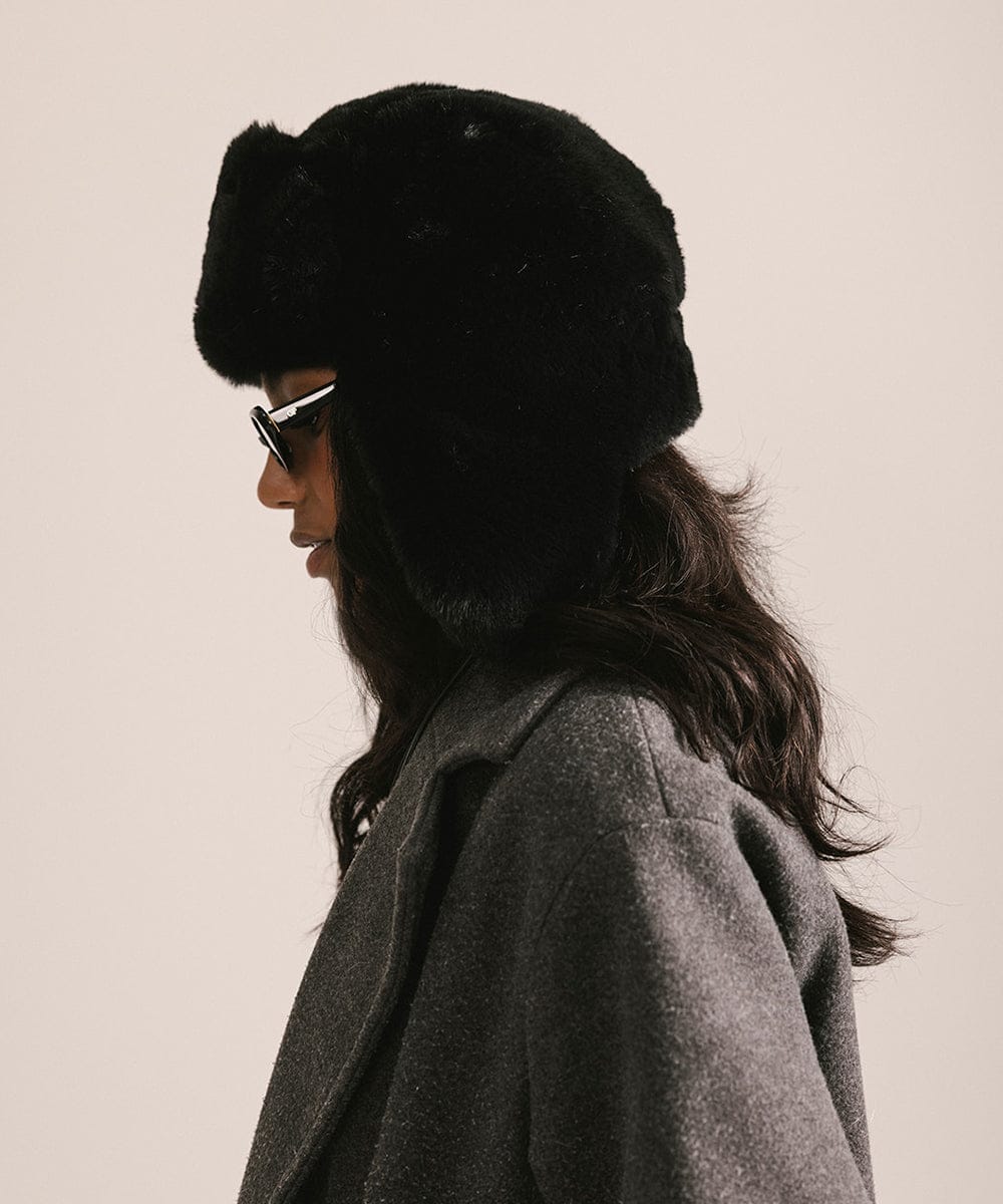Person wearing a black fur hat and sunglasses with a neutral background #color_black