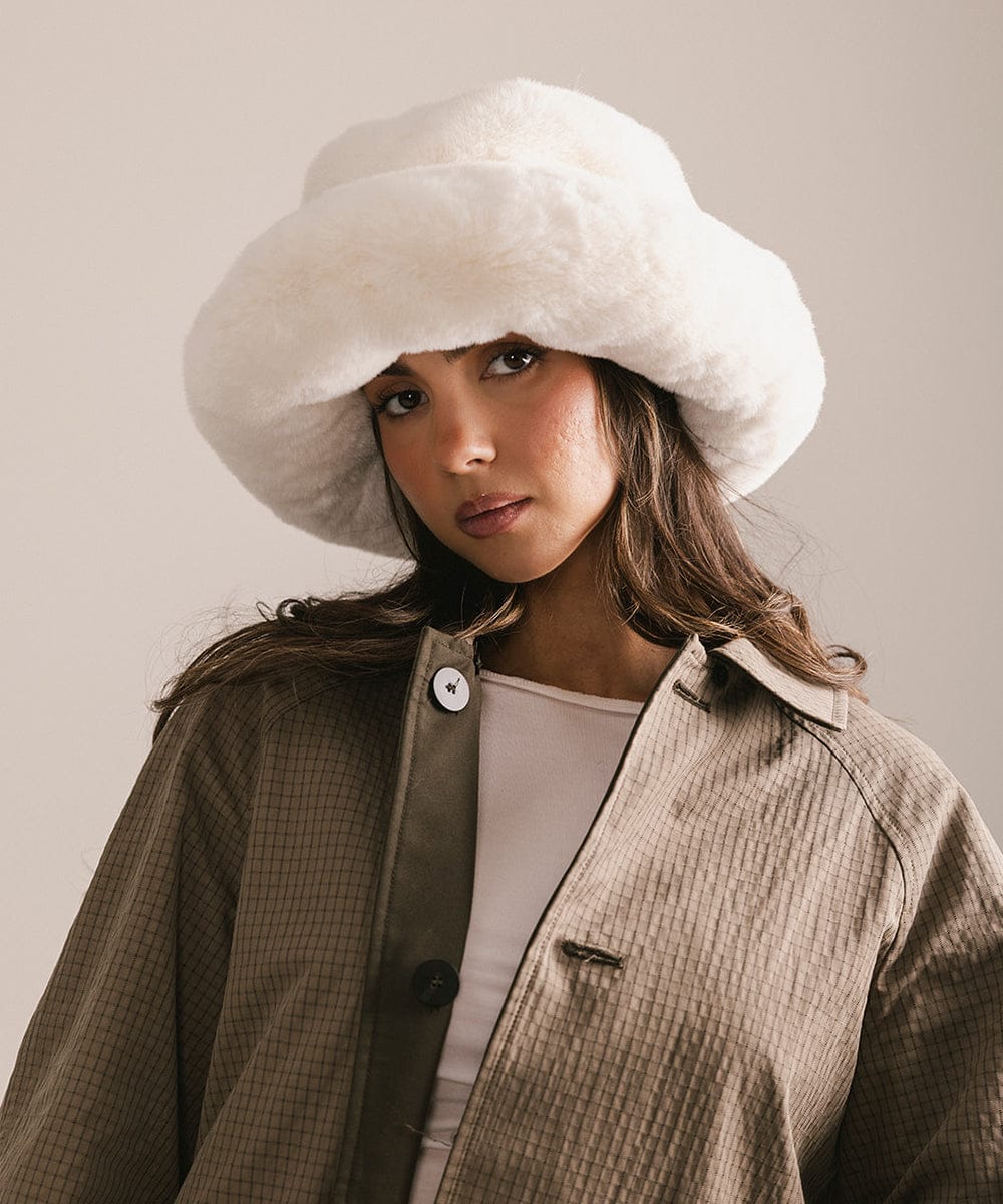 Woman wearing a large white fur hat against a neutral background #color_winter white