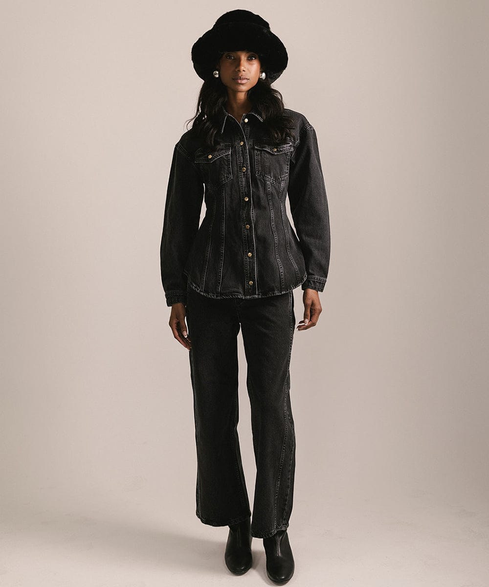 Person wearing a black denim jacket, pants, and hat on a beige background #color_black