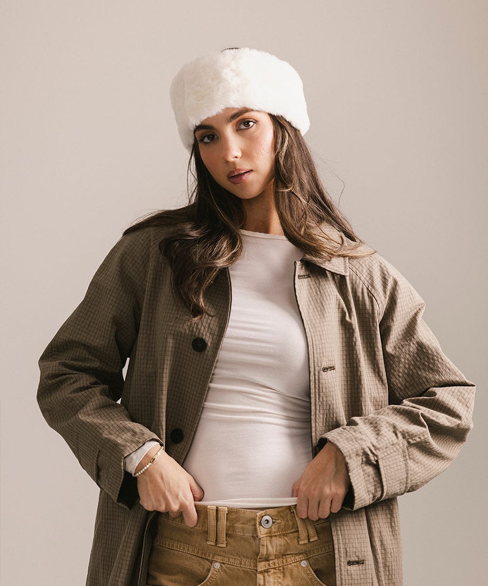 Woman wearing a beige coat, white beanie, and white shirt against a plain background #color_winter white