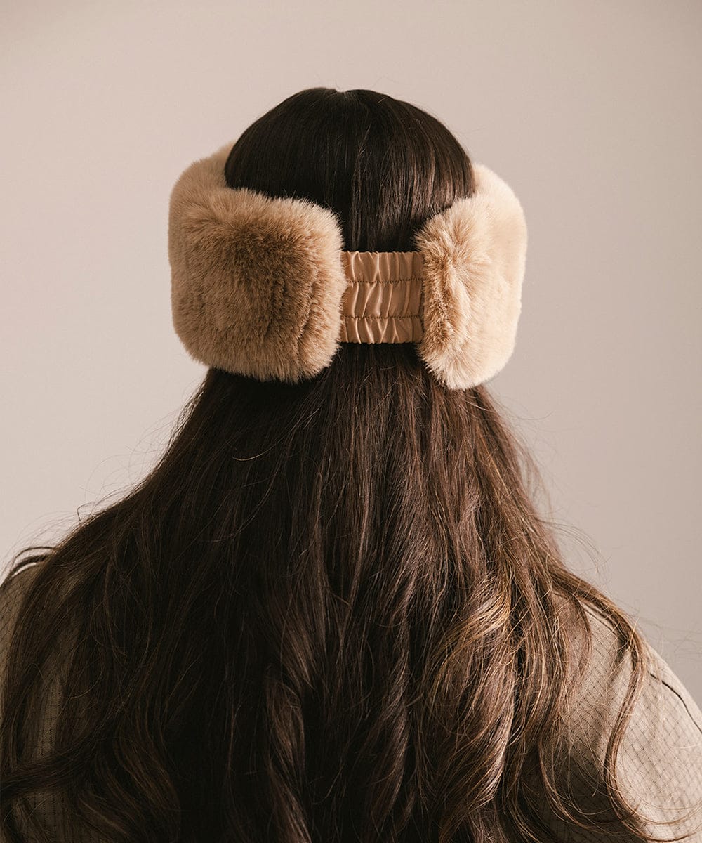 Person wearing beige fur ear muffs with a neutral background #color_tan