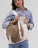 Woman wearing a denim shirt carrying a hat on a natural colored canvas tote bag against a plain background #color_natural