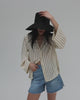 Woman wearing a black oversized raffia straw bucket hat, a light colored shirt and blue shorts, posing against a plain background #color_black 
