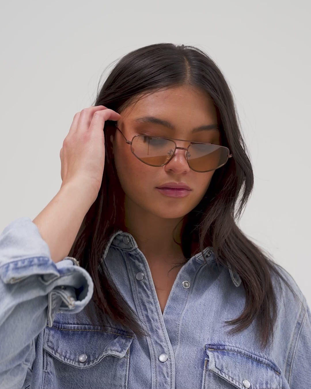 Woman wearing brown sunglasses and a denim shirt, posing against a plain background #color_brown