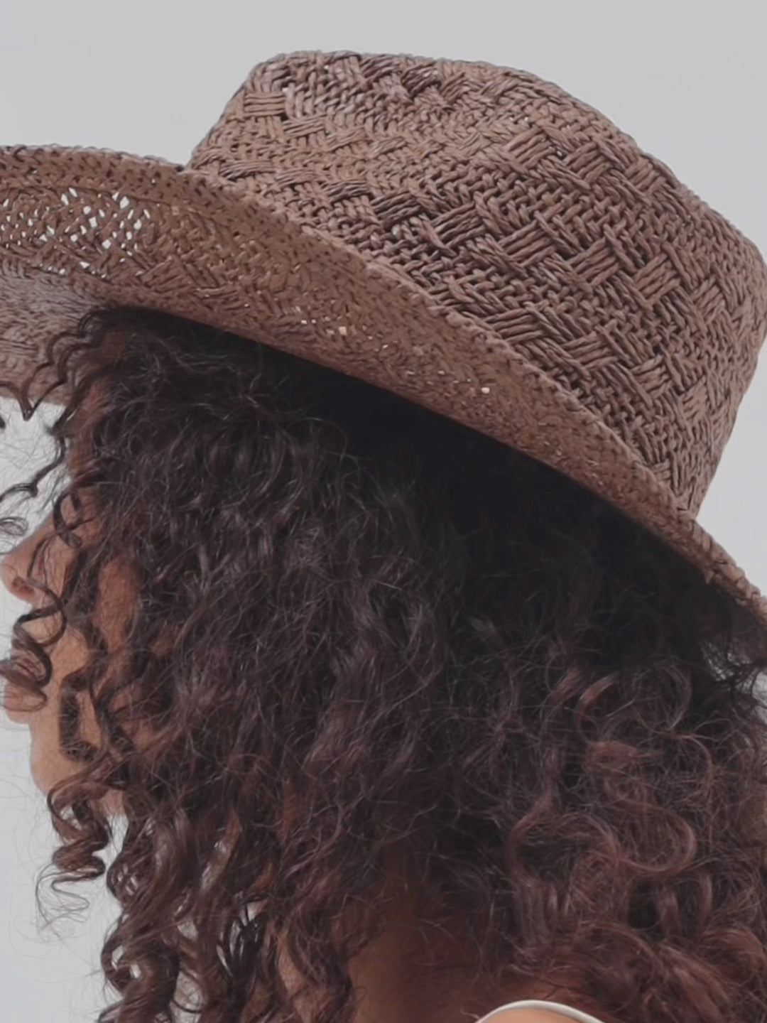 Woman wearing a brown straw hat with a decorative band against a white background #color_chocolate