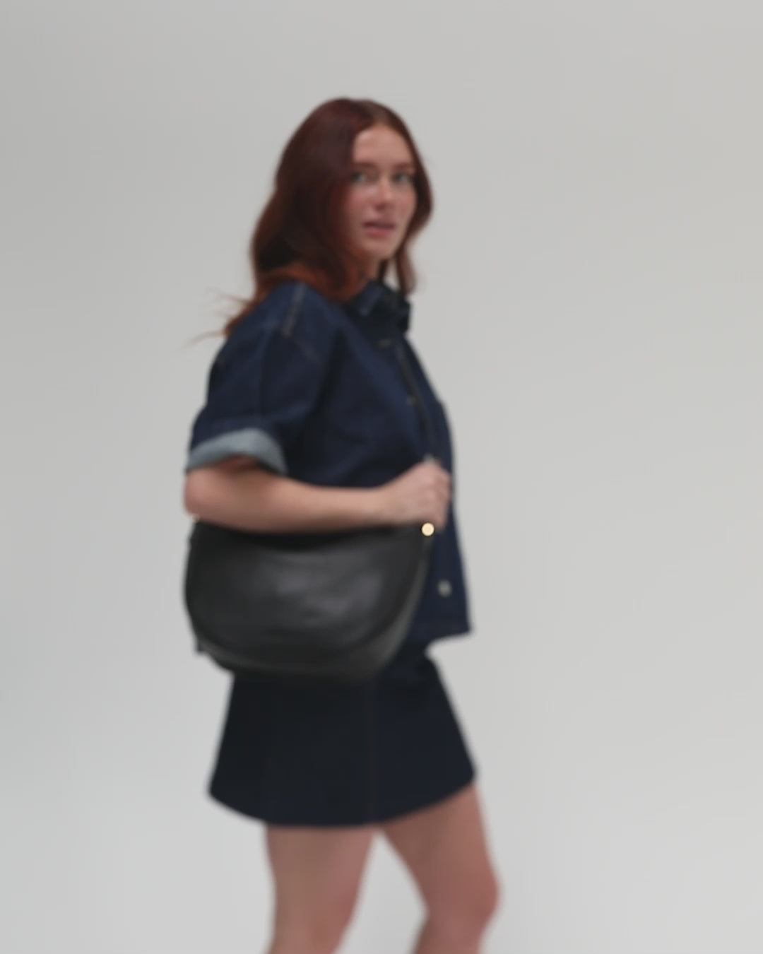 Person wearing a denim shirt and denim skirt, carrying a black genuine leather slouchy bag against a plain background #color_black