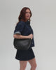 Person wearing a denim shirt and denim skirt, carrying a black genuine leather slouchy bag against a plain background #color_black