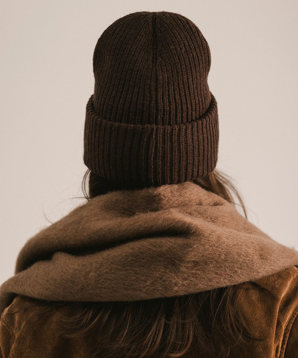 Person wearing a brown knit beanie and coat against a beige background #color_brown