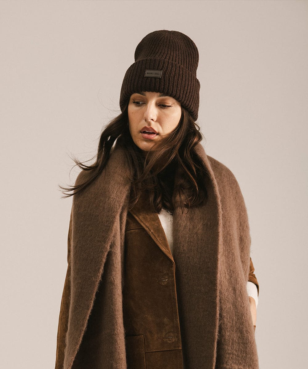 Woman wearing a brown coat and beanie against a neutral background #color_brown