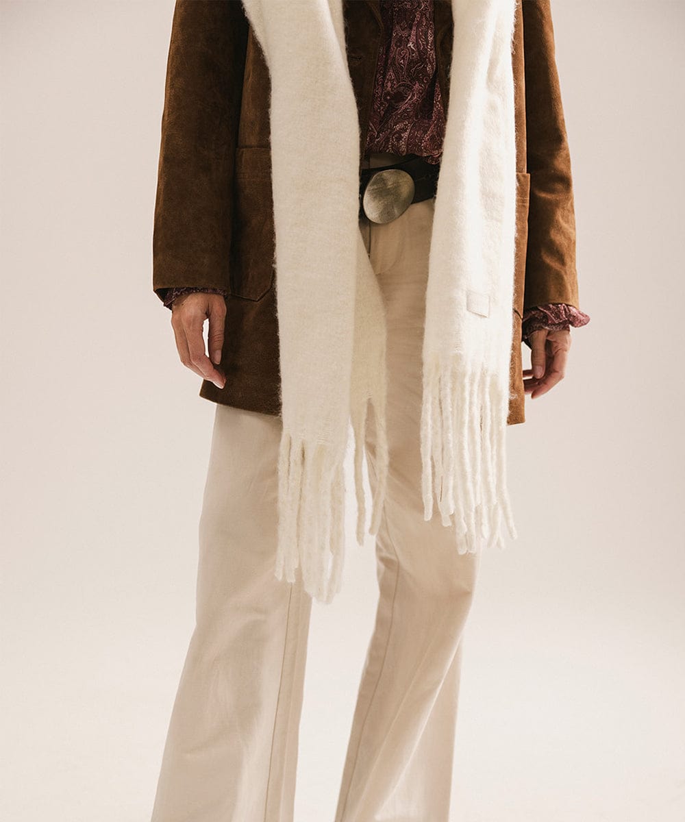 Person wearing a brown coat with a white fringed scarf on a plain background #color_off white