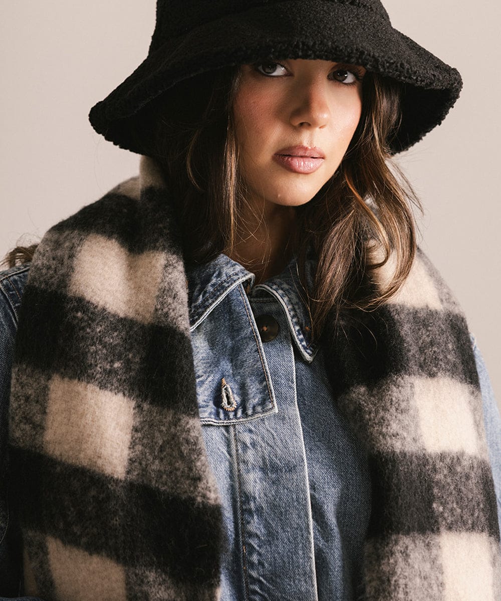 Person wearing a black hat, plaid coat, and denim jacket against a neutral background #color_Black - Cream Buffalo Check