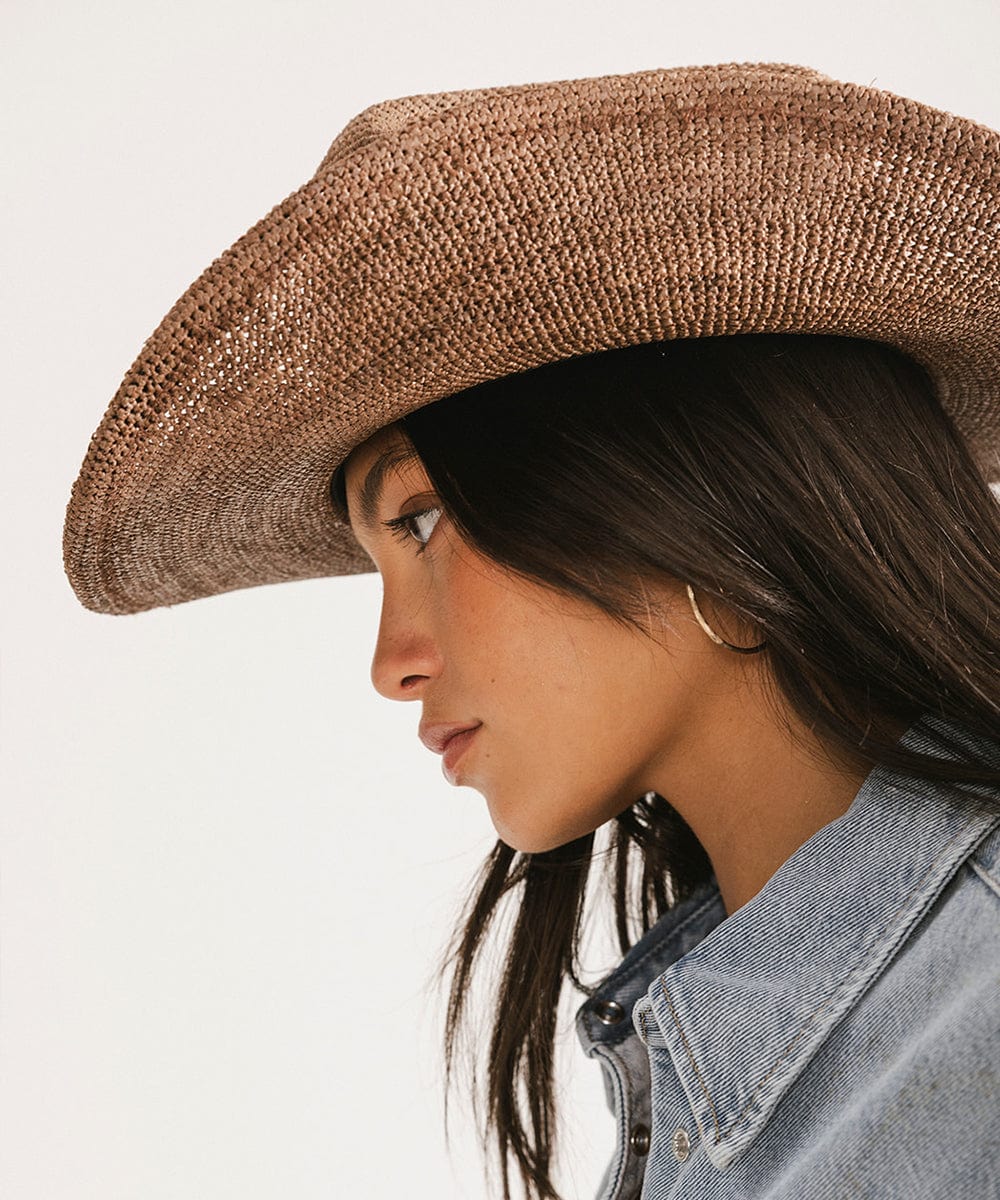 Woman wearing a chocolate colored straw cowboy hat and a denim shirt, facing sideways against a plain background #color_chocolate