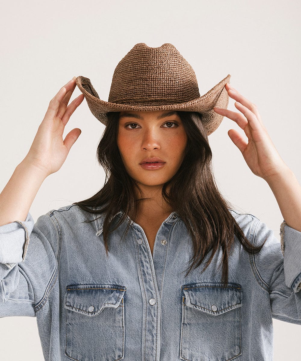 Woman wearing a chocolate colored straw cowboy hat and a denim shirt against a plain background #color_chocolate