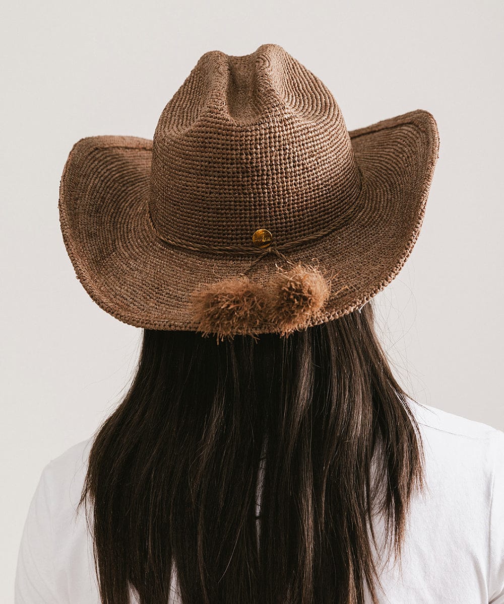 Woman wearing a chocolate colored straw cowboy hat with a band and a white t-shirt, facing behind against a plain background #color_chocolate