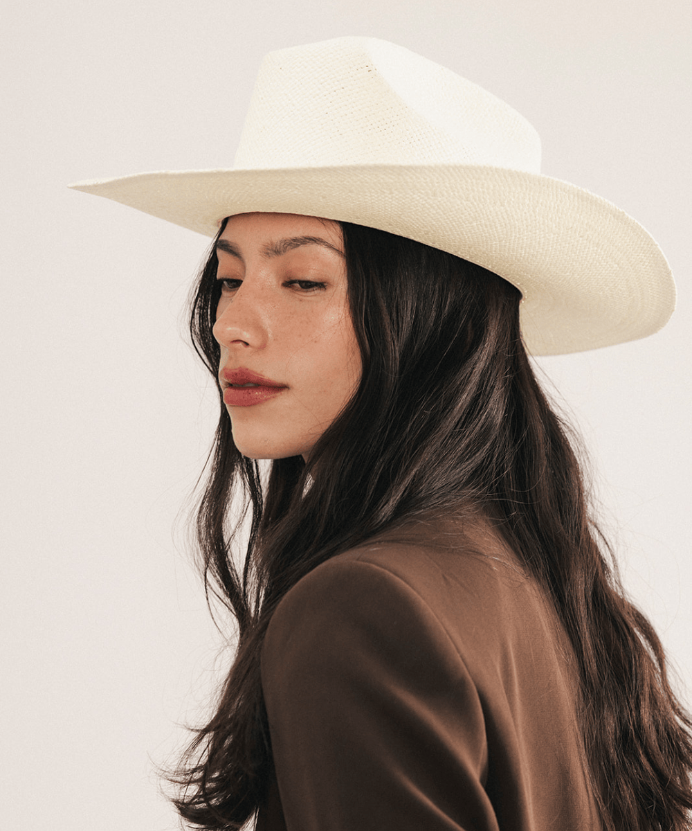 Woman wearing a white straw cowboy hat and dark clothing against a plain background #color_natural white