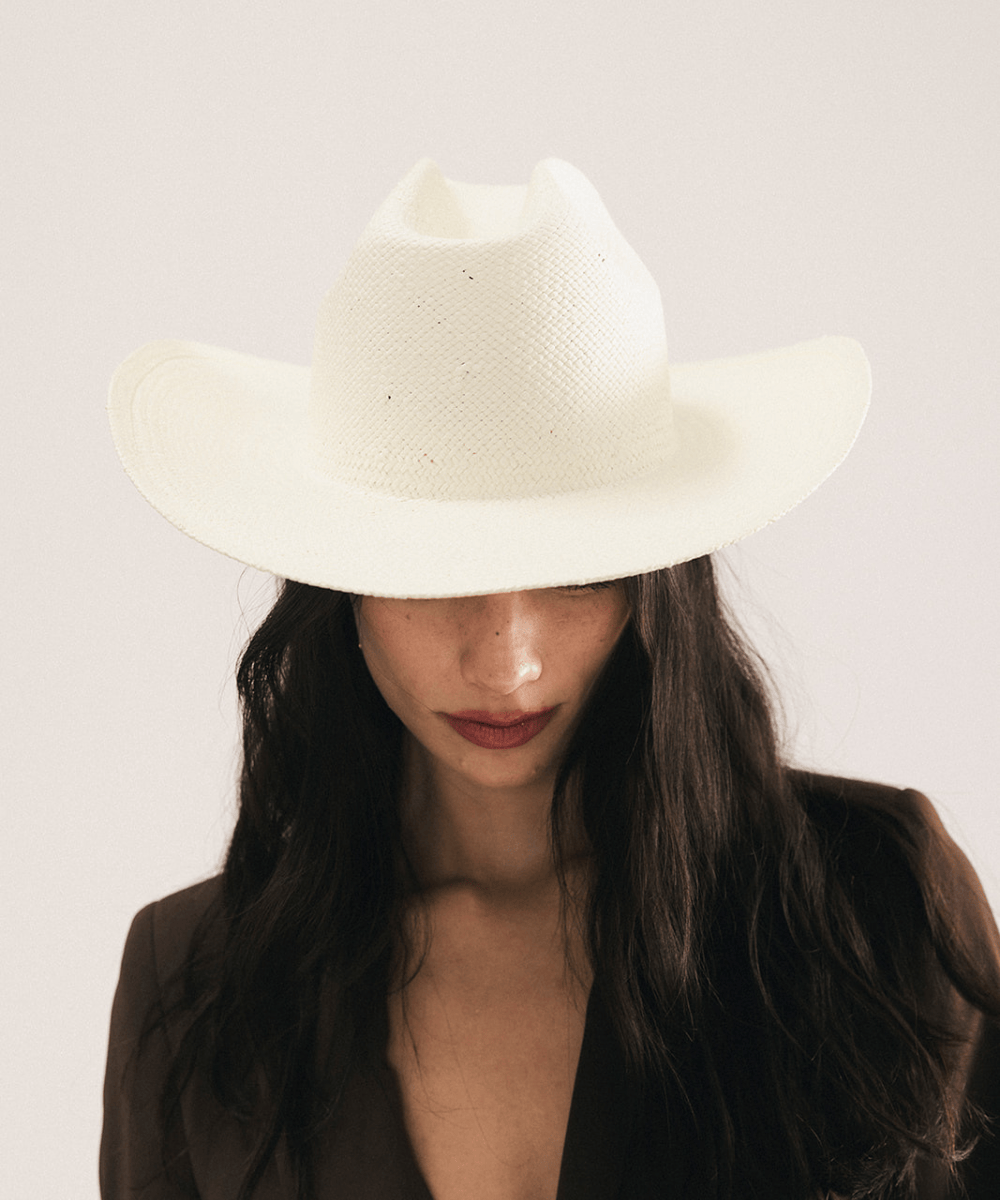 Woman wearing a white straw cowboy hat and dark clothing against a plain background #color_natural white