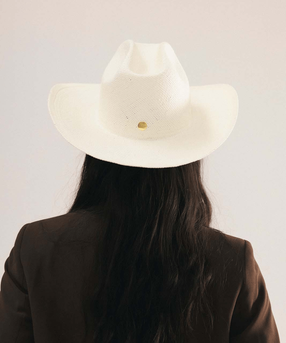 Woman wearing a white straw cowboy hat and dark clothing against a plain background #color_natural white