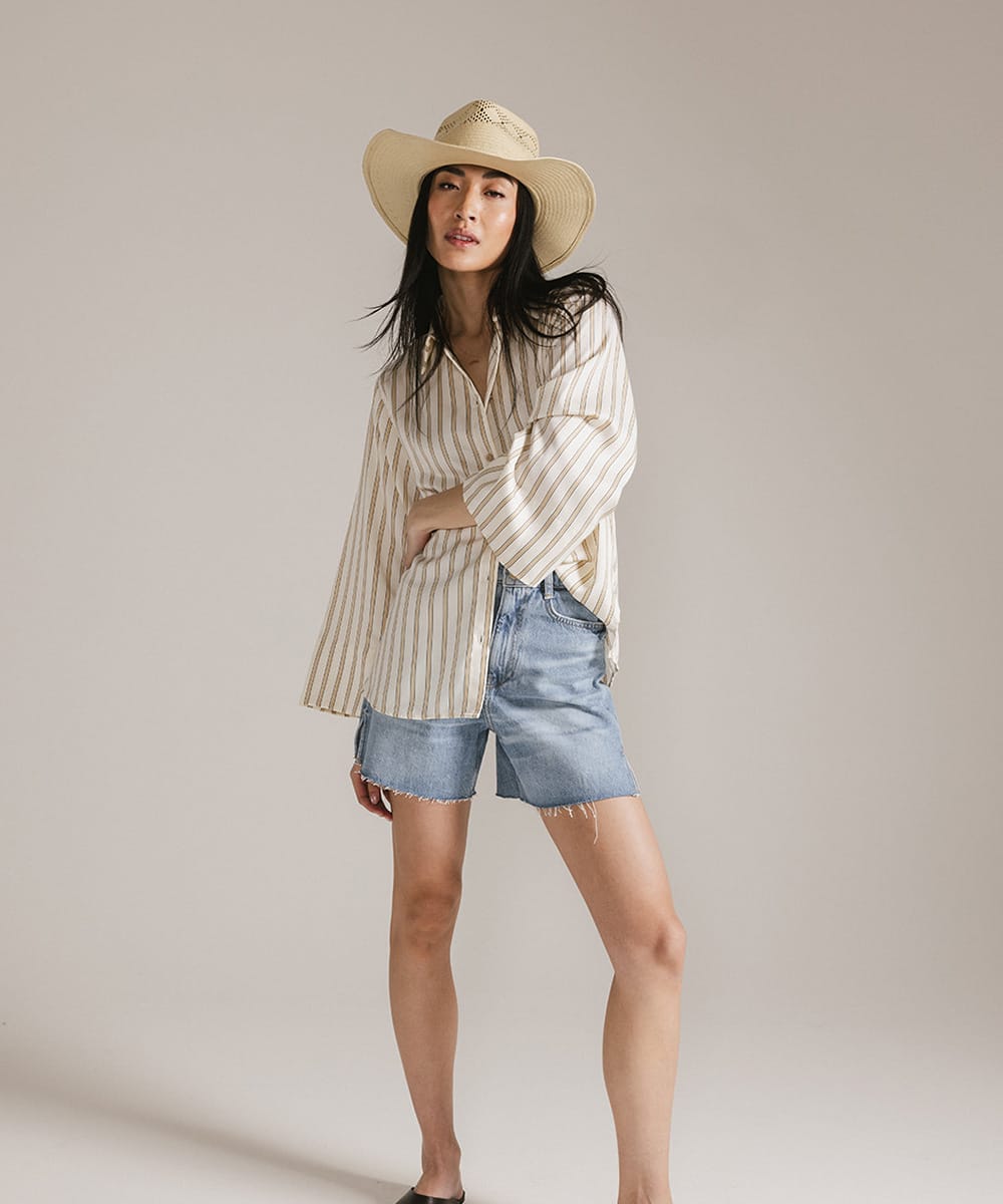 Woman wearing a striped shirt, denim shorts, and a hat against a plain background #color_natural