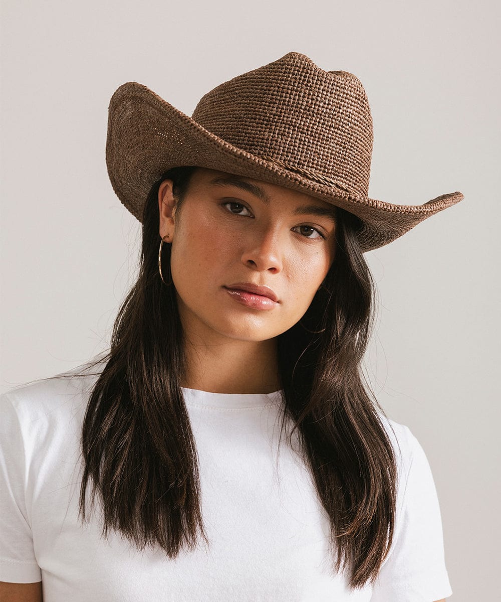 Woman wearing a chocolate colored straw cowboy hat and a white t-shirt against a plain background #color_chocolate