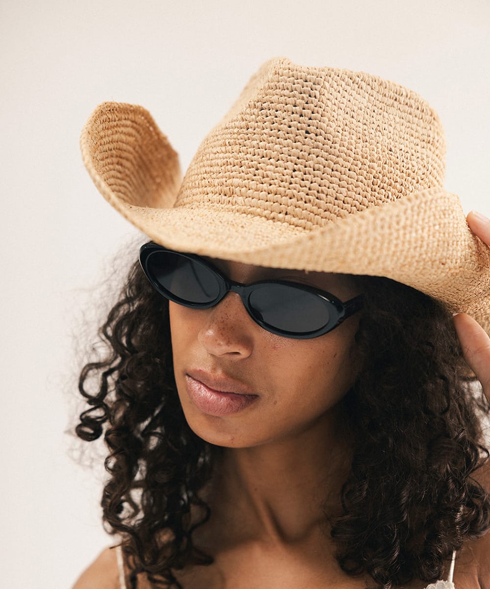 Woman wearing a straw hat and black sunglasses against a plain background #color_natural