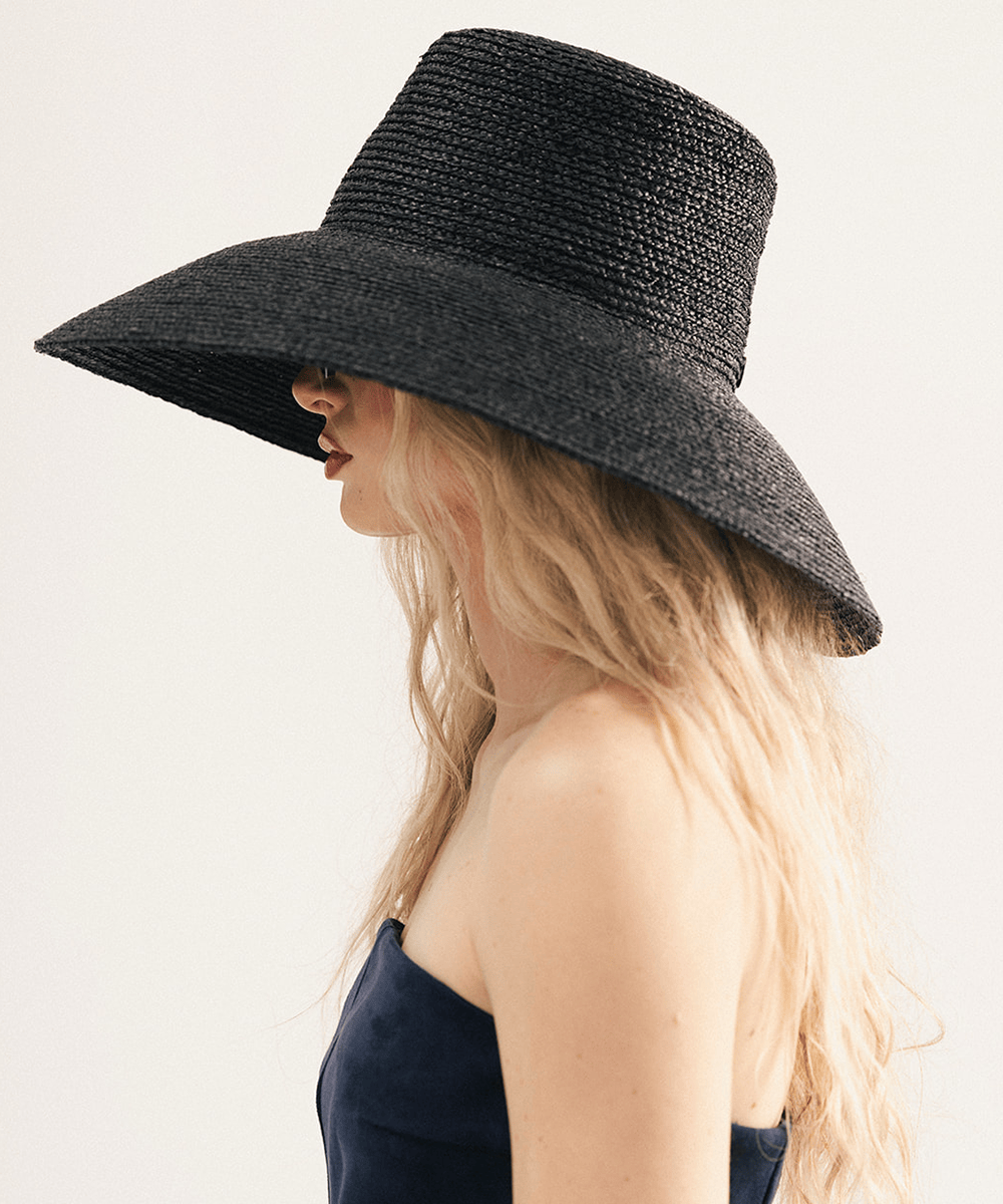 Woman wearing a black oversized raffia straw bucket hat with a wide brim on a white background #color_black