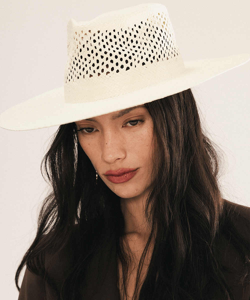 Woman wearing a natural white straw fedora hat with a wide brim and intricate venting details. #color_natural white