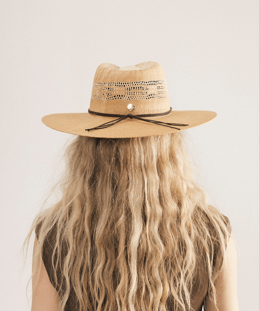 Woman wearing a washed tan straw fedora hat and dark clothing against a plain background #color_washed tan
