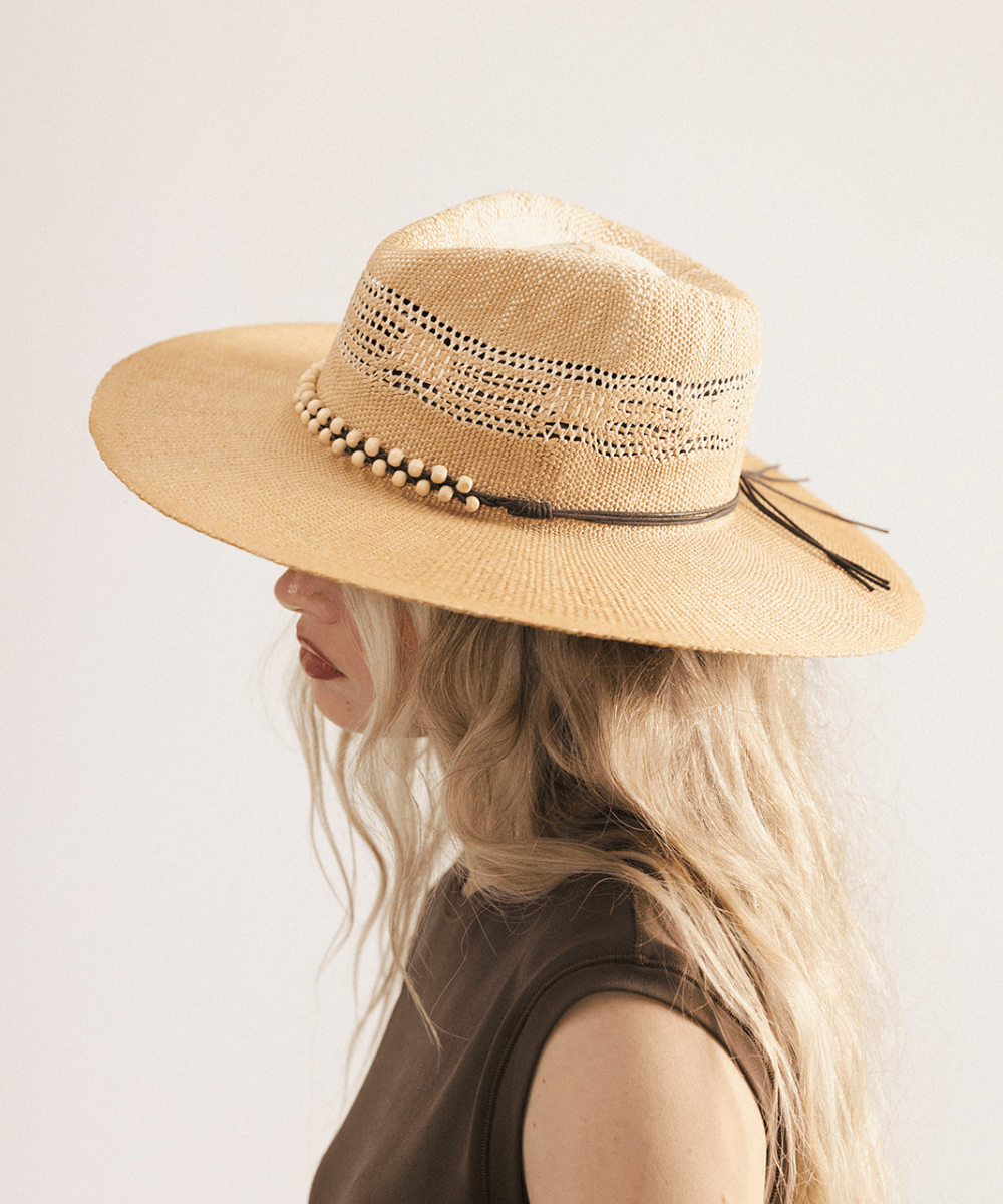 Woman wearing a washed tan straw fedora hat and dark clothing against a plain background #color_washed tan