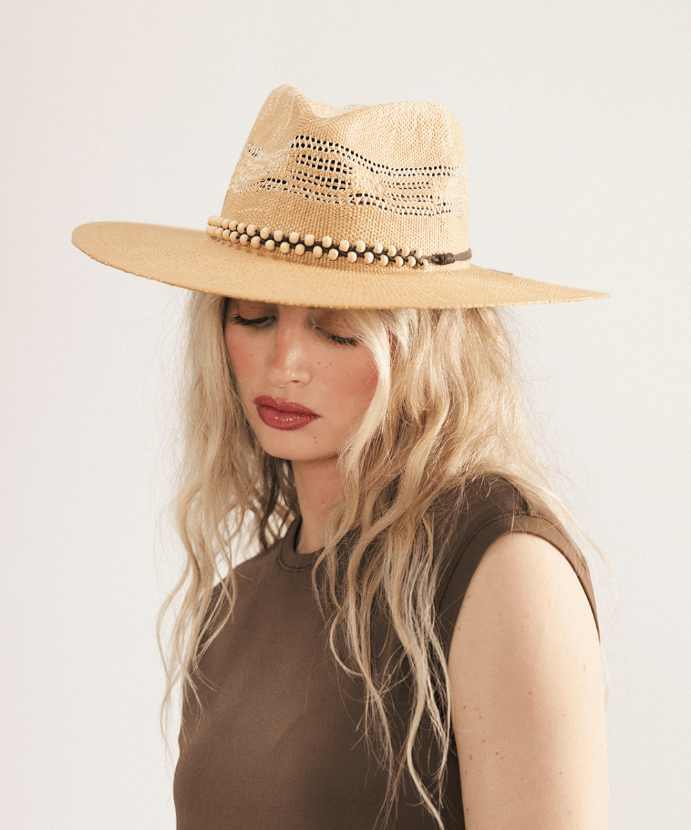 Woman wearing a washed tan straw fedora hat and dark clothing against a plain background #color_washed tan