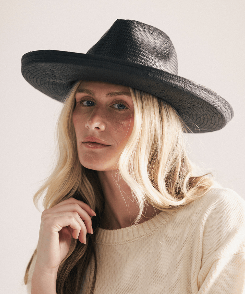 Woman wearing a black pencil brim fedora hat made of paper straw, displayed against a white background. #color_black