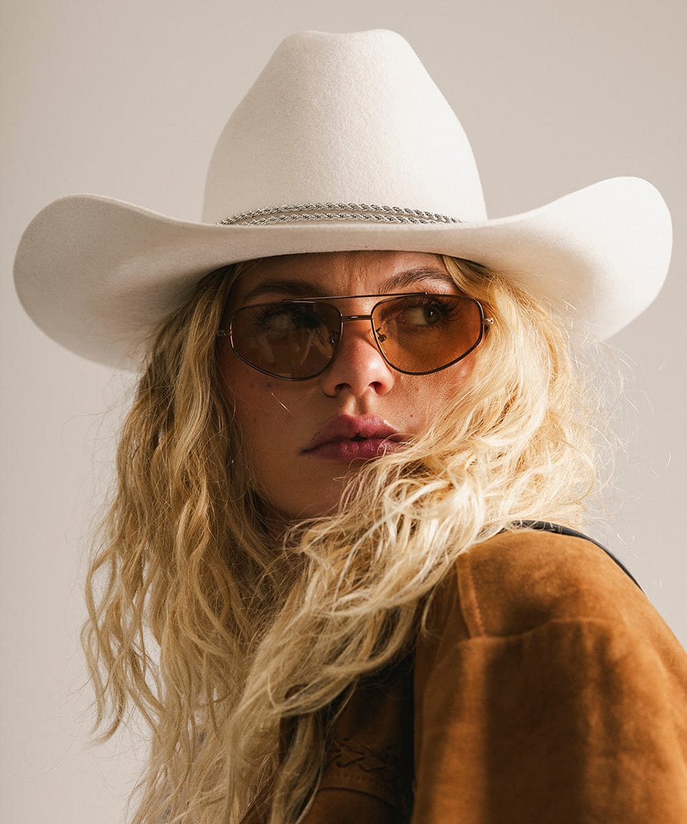Person wearing a white cowboy hat and brown sunglasses against a neutral background #color_brown