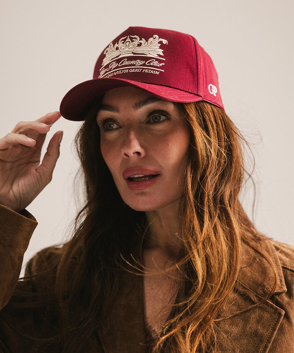 Woman wearing a burgundy vintage trucker cap with a white logo and a brown coat against a plain background  #color_burgundy