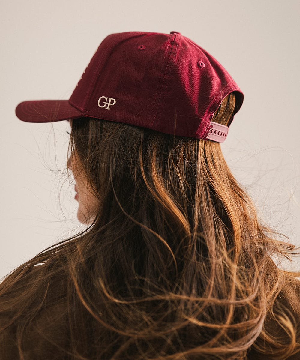 Person wearing a burgundy trucker cap with a logo, facing away from the camera against a plain background #color_burgundy