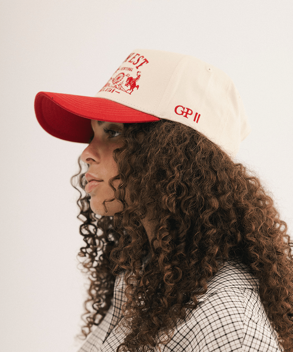 Woman's side view wearing a red and white baseball cap and plaid shirt in a white background #color_cream - rust red