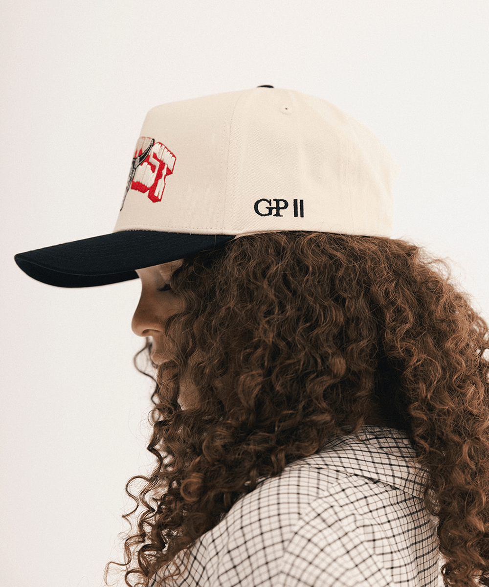Woman's side view wearing a beige and black cap with bull logo on a white background #color_cream - black