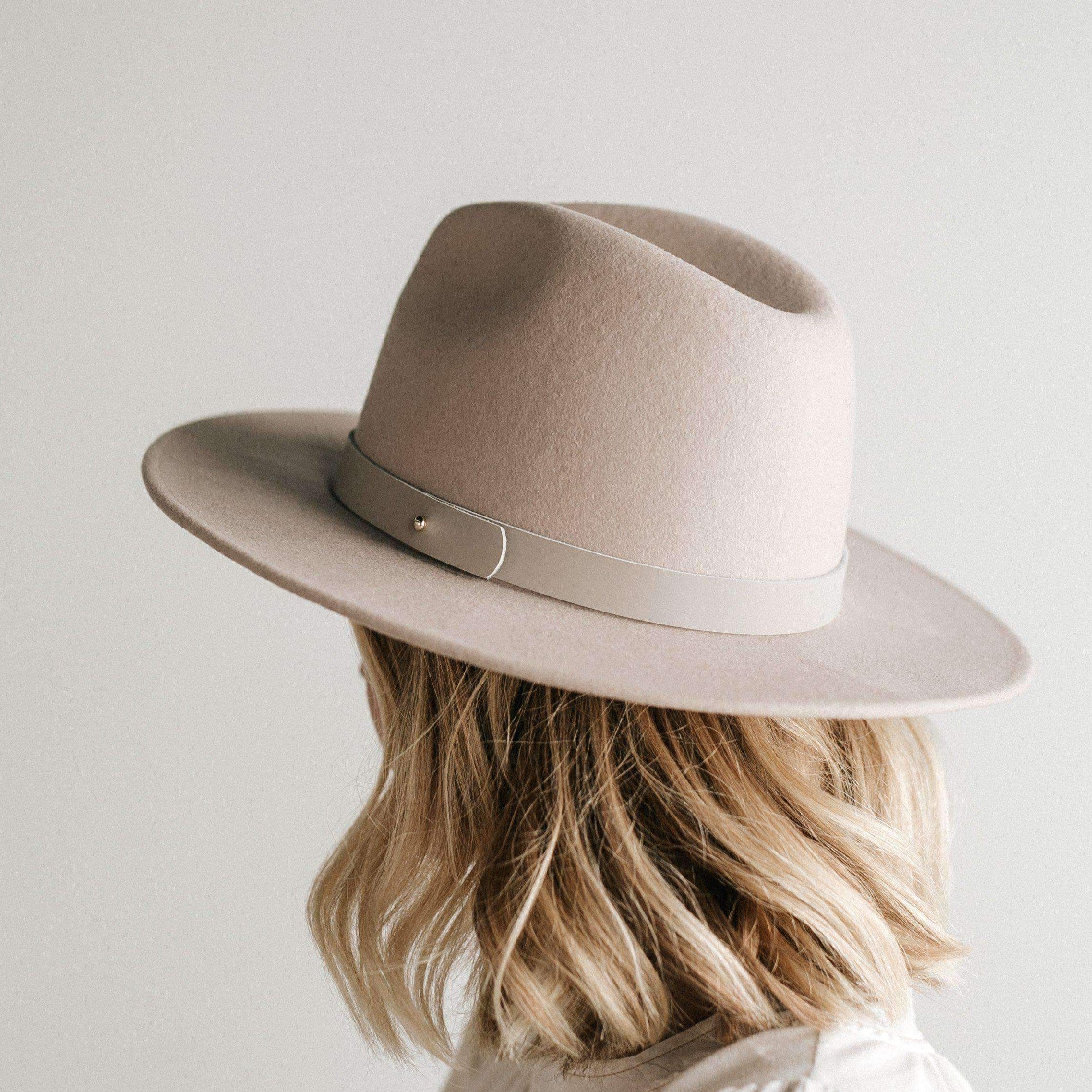 Woman wearing an ivory colored fedora hat with a hat band facing behind against a plain background #color_ivory