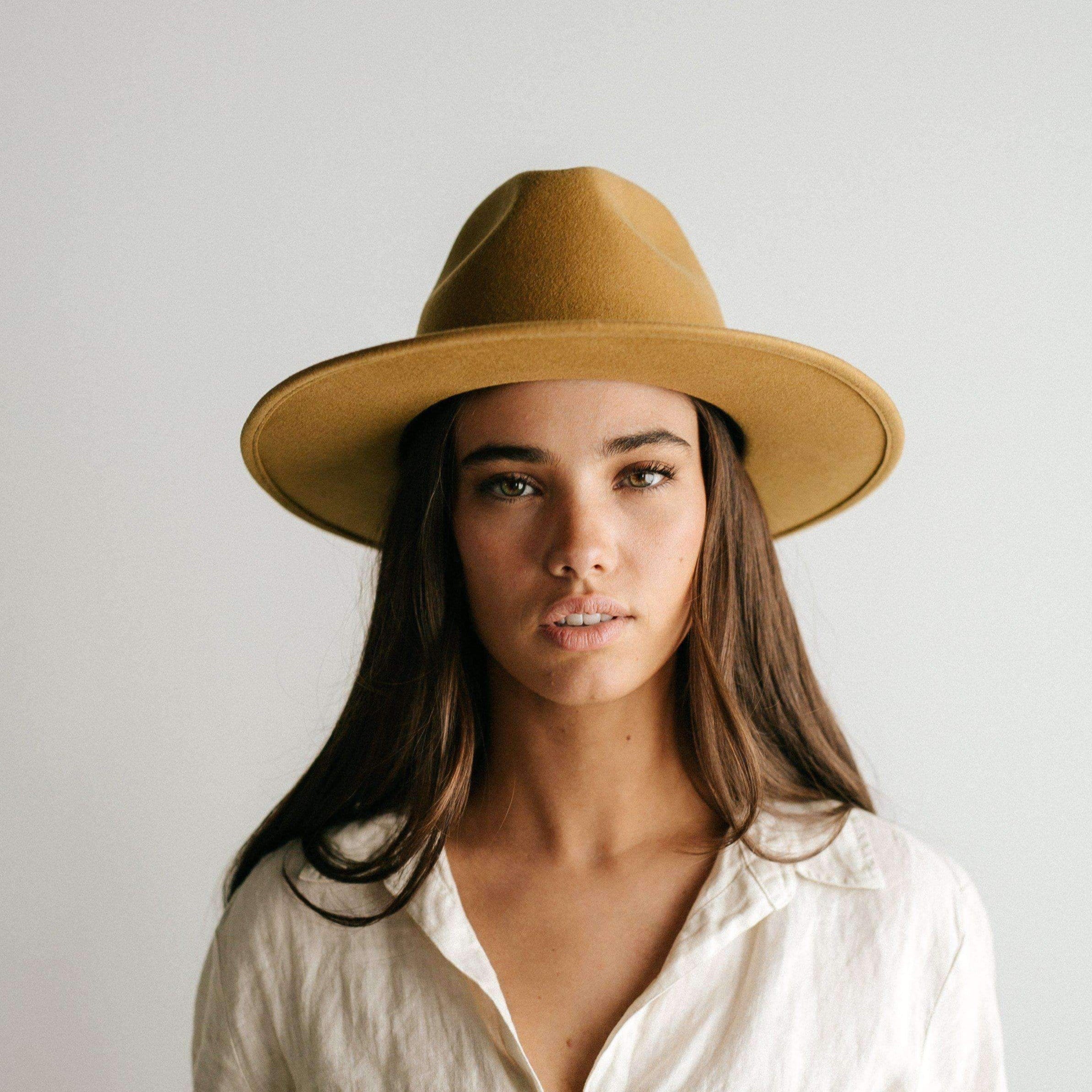 Woman wearing a mustard colored fedora hat and a white shirt against a plain background #color_mustard