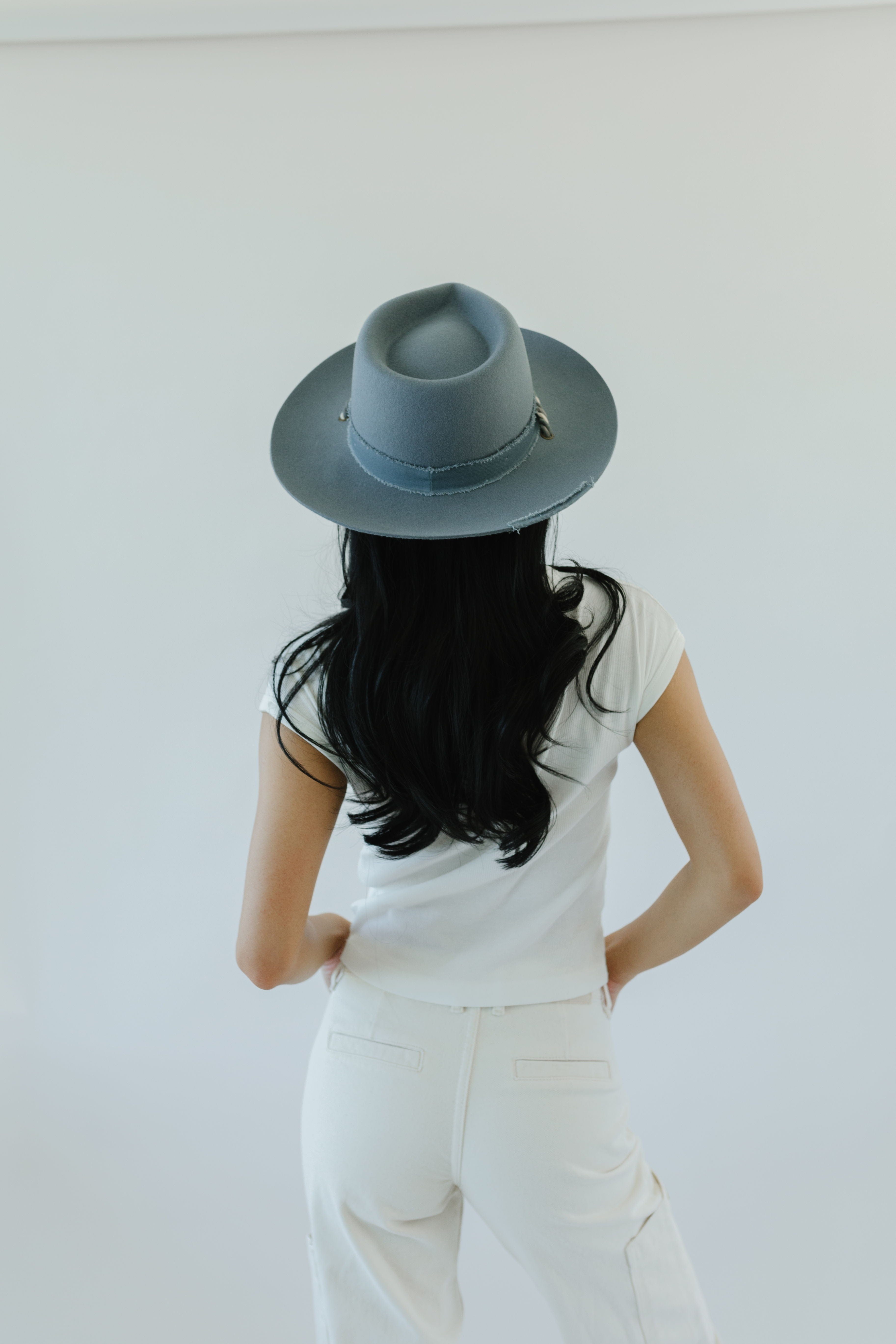 Woman wearing a denim colored wide brim hat, a white t-shirt and white pants against a plain background  #color_denim