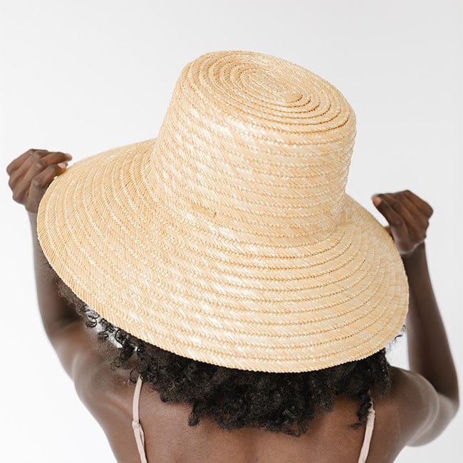 Woman wearing a natural colored boater-style straw hat facing behind against a plain background #color_natural